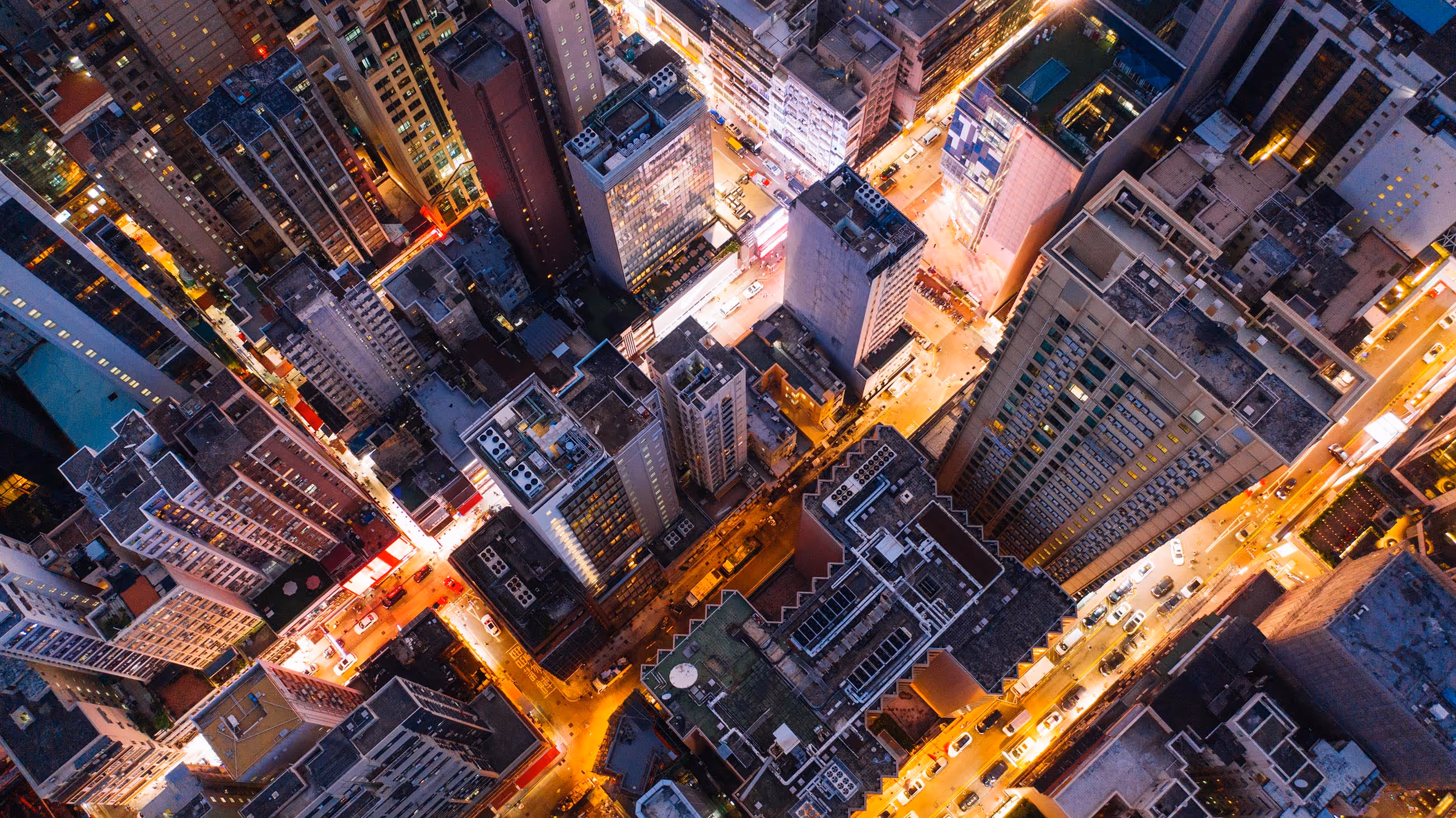 Aerial view of a city at night with tall buildings and brightly lit streets in a grid pattern.