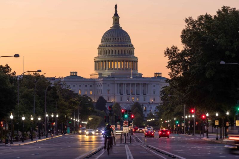 The U.S. Capitol building at dusk with cars and a cyclist on the street ahead.