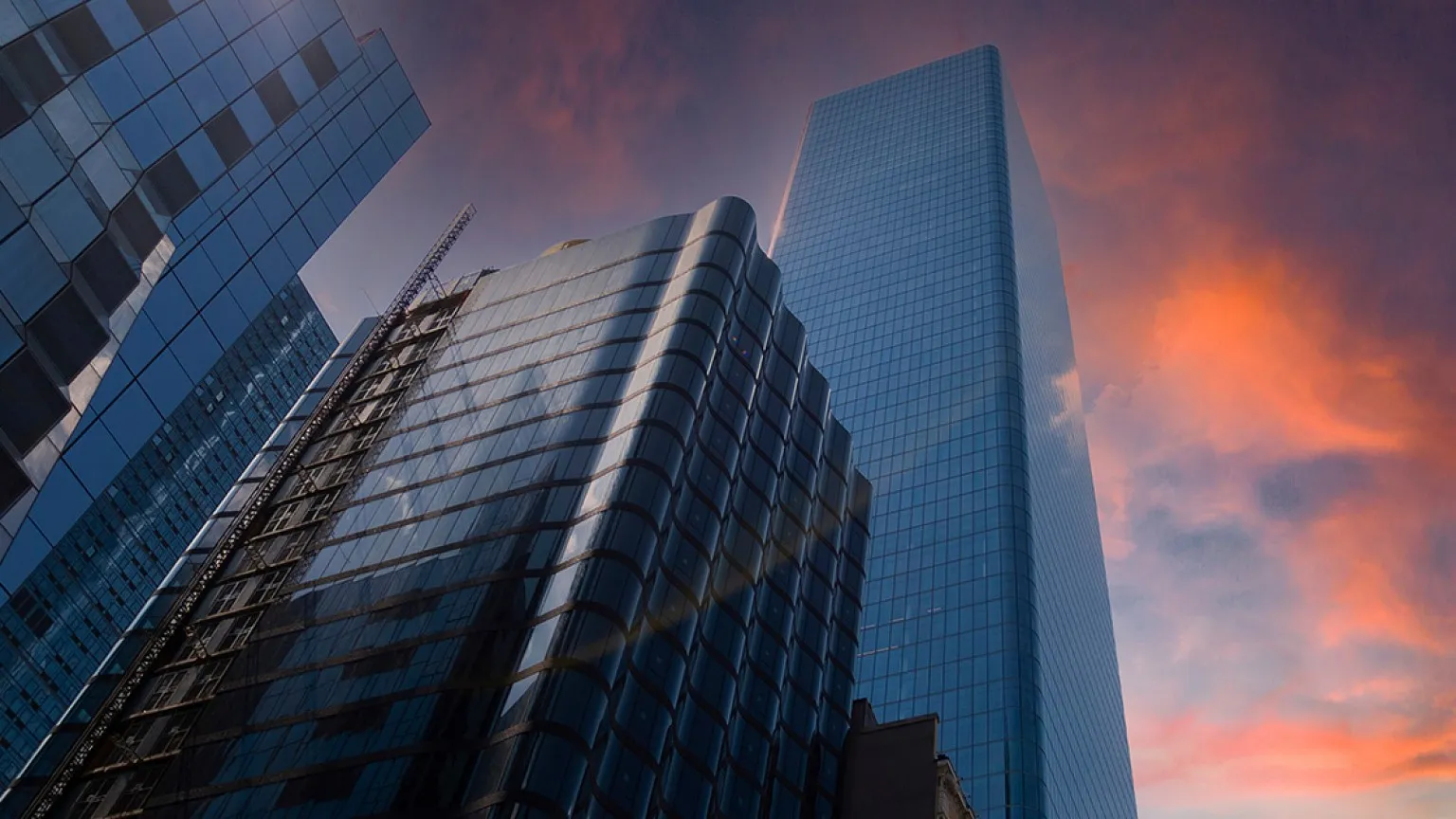 Modern glass skyscrapers reflecting the colorful sunset sky in a cityscape.