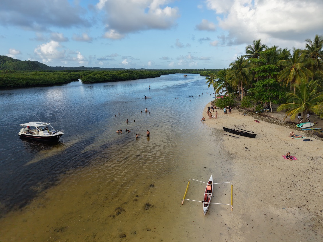 Vue aérienne par drone d’une plage tropicale de Siargao, avec ses eaux cristallines, ses cocotiers et ses embarcations traditionnelles philippines.