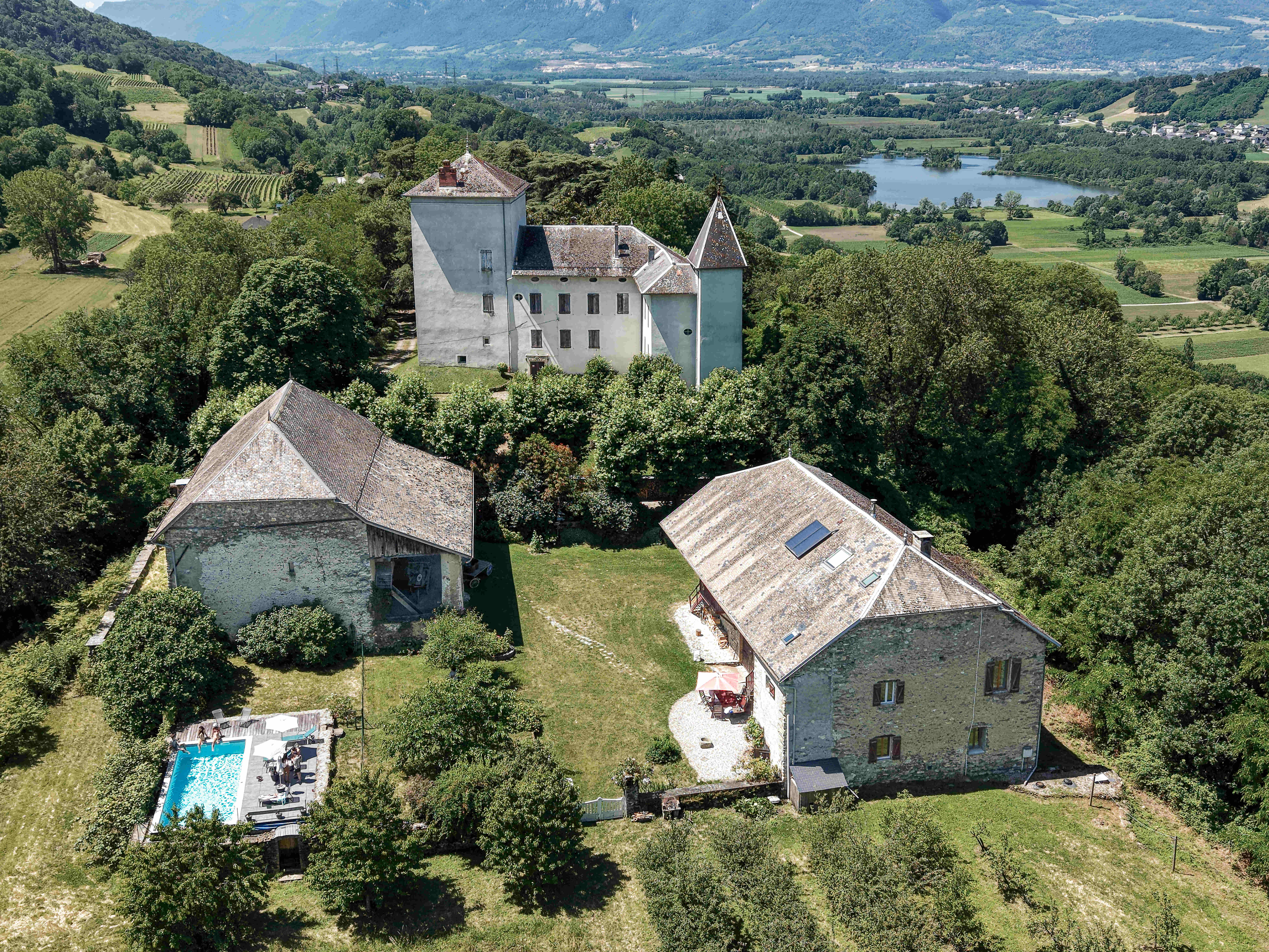 Vue aérienne d'une propriété de caractère composée de bâtiments en pierre, entourée d'un vaste jardin arboré avec piscine, dans un environnement naturel.
