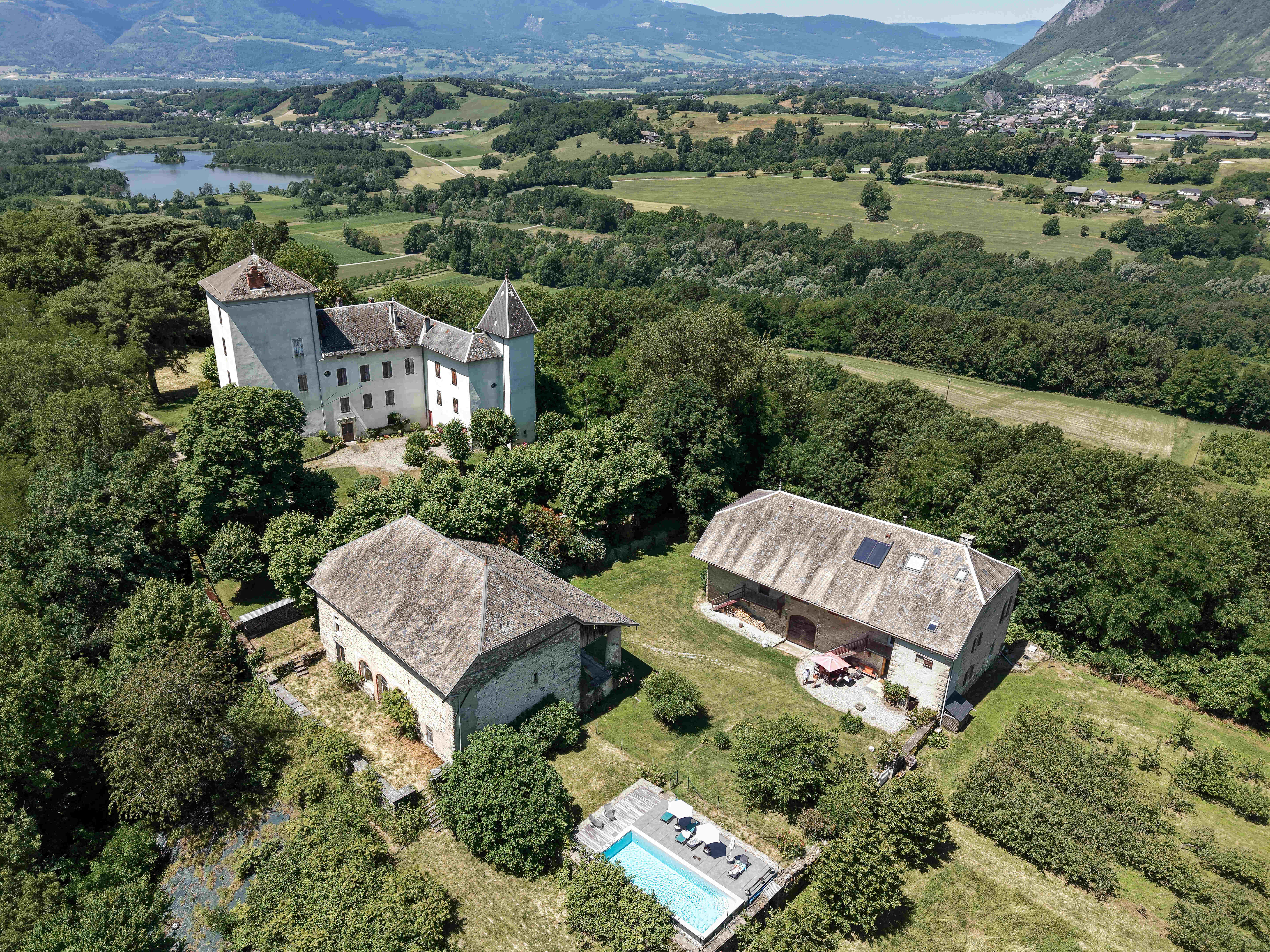 Vue aérienne menant en valeur l'architecture de la propriété, ses bâtiments en pierre, sa piscine et son environnement paysager.