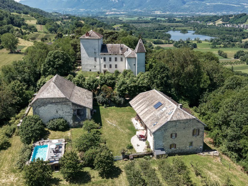 Vue aérienne de l'ensemble de la propriété, avec le château, les bâtiments en pierre, les jardins et la piscine.
