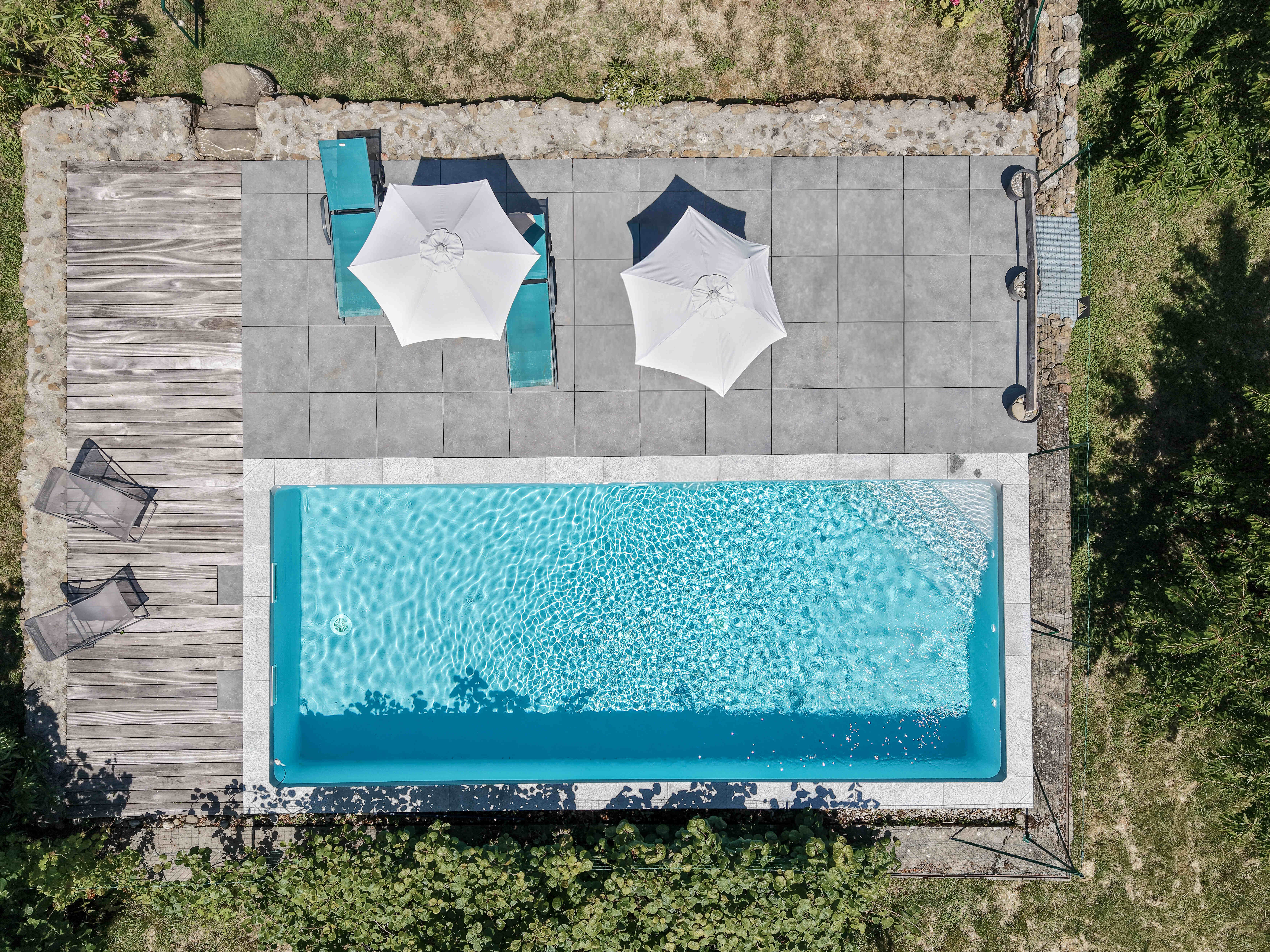 Vue aérienne de la piscine extérieure et de sa terrasse aménagée avec transats et parasols.