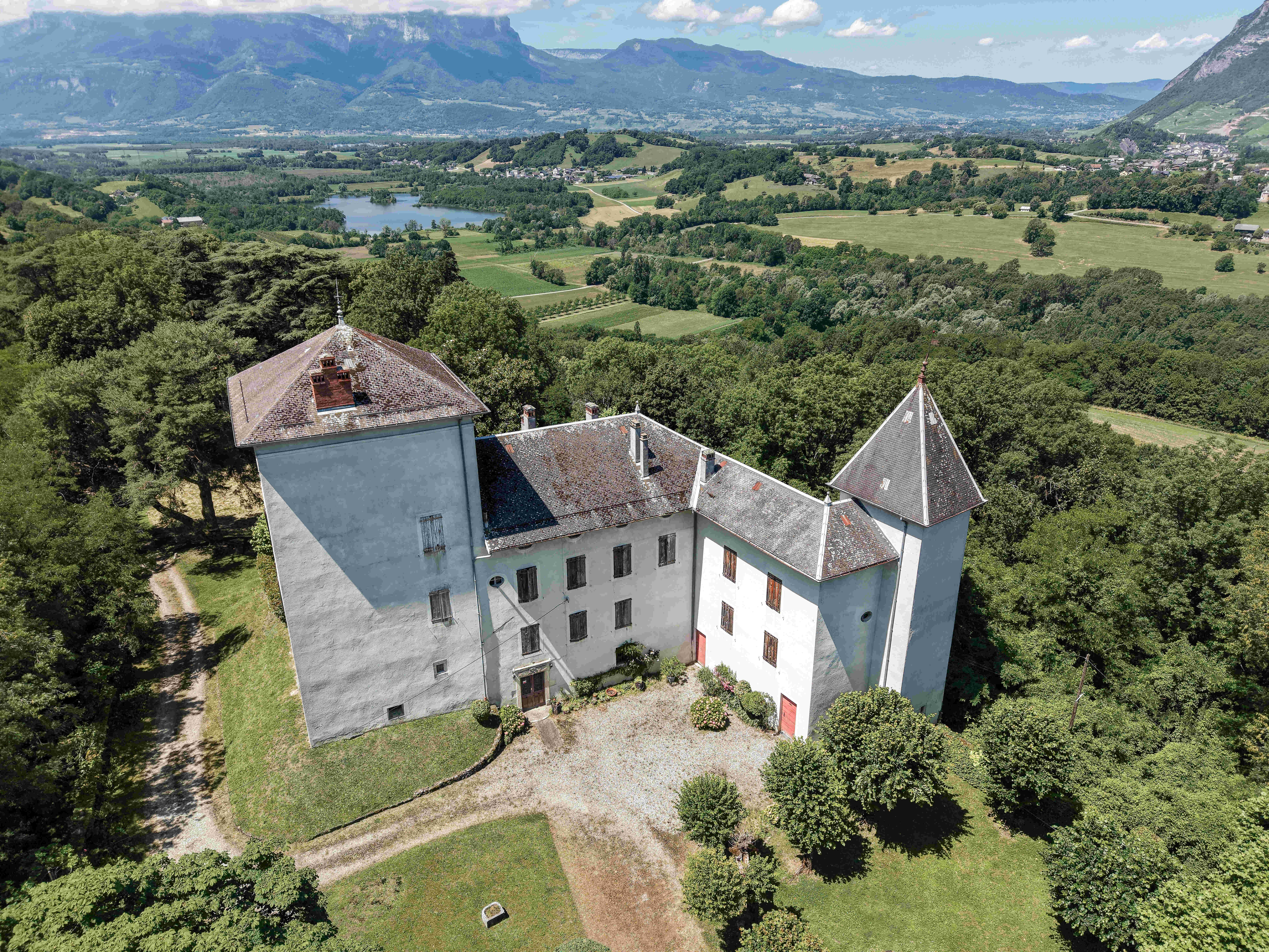 Vue aérienne rapprochée du château et de son architecture traditionnelle, avec la vallée les montagnes en arrière plan.