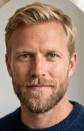 Portrait of a man with short blonde hair, blue eyes, and a trimmed beard wearing a dark blue sweater.