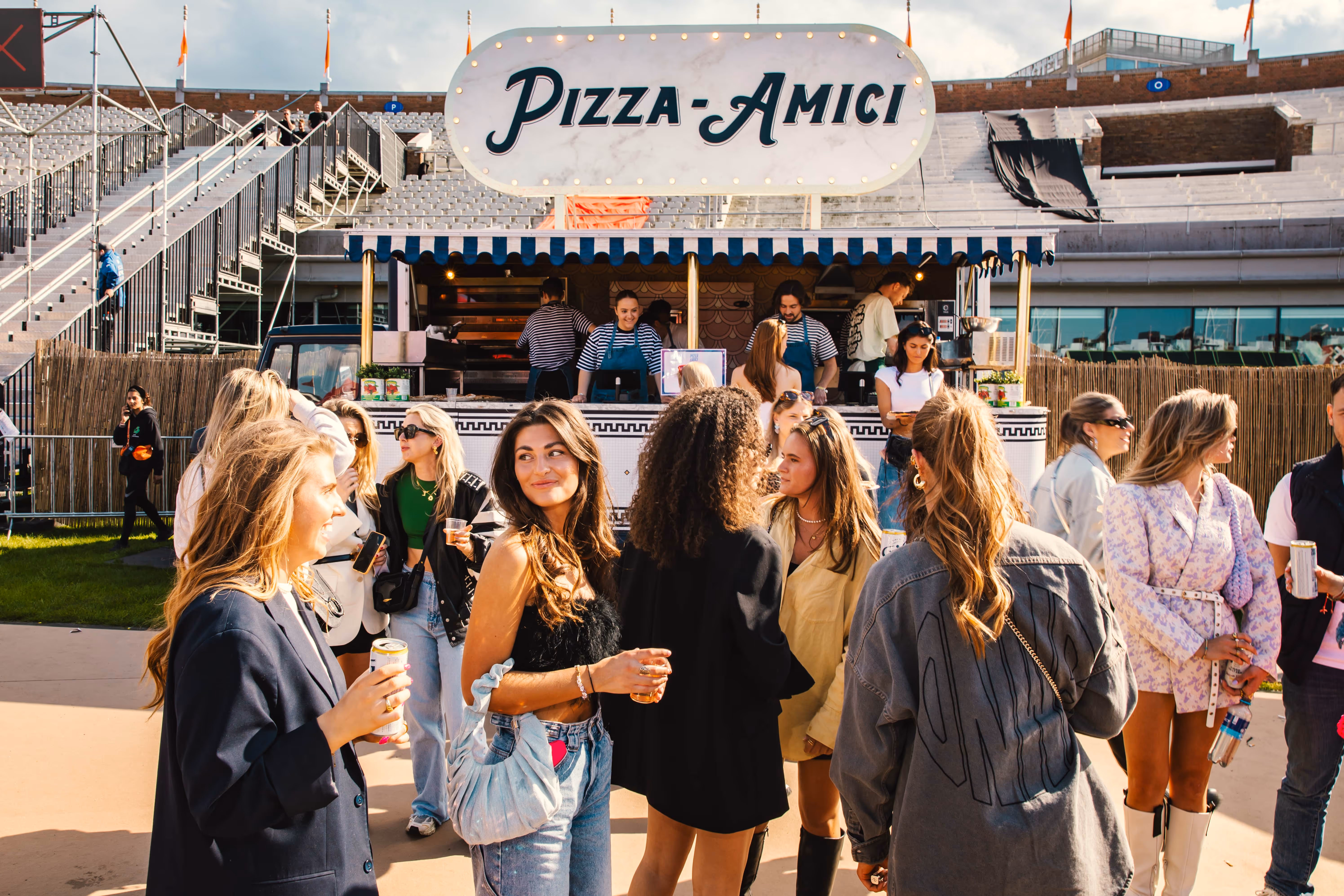 Medewerkers in gestreepte shirts en denim schorten bereiden en verkopen pizza's aan een marmeren toonbank met een menubord met Margherita en Salame pizza's.