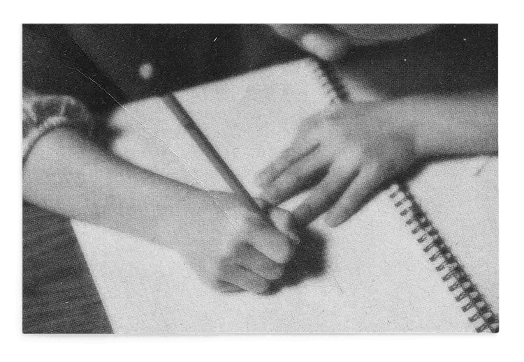 Black and white photo of a child holding a pencil and writing in a notebook.