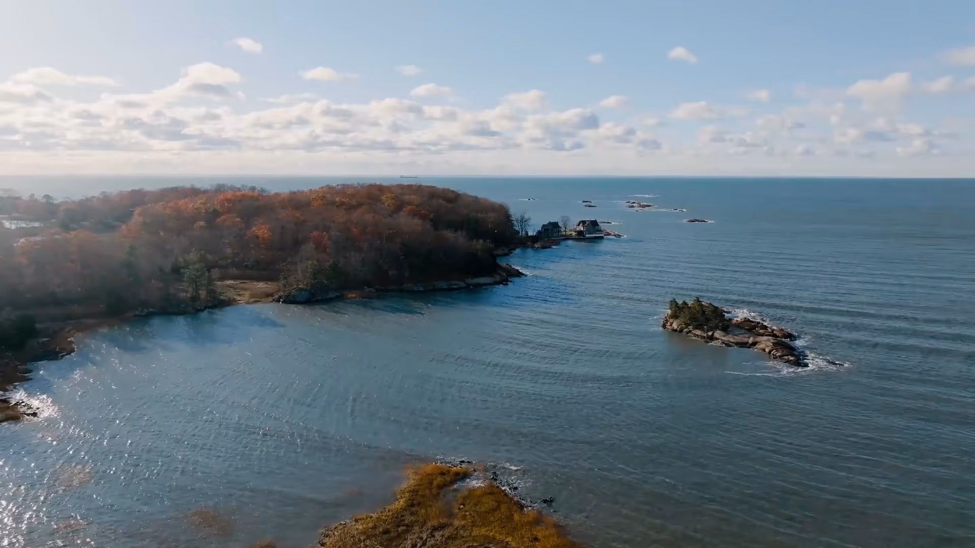 Aerial view of a coastal area with small wooded islands and calm ocean water under a partly cloudy sky.