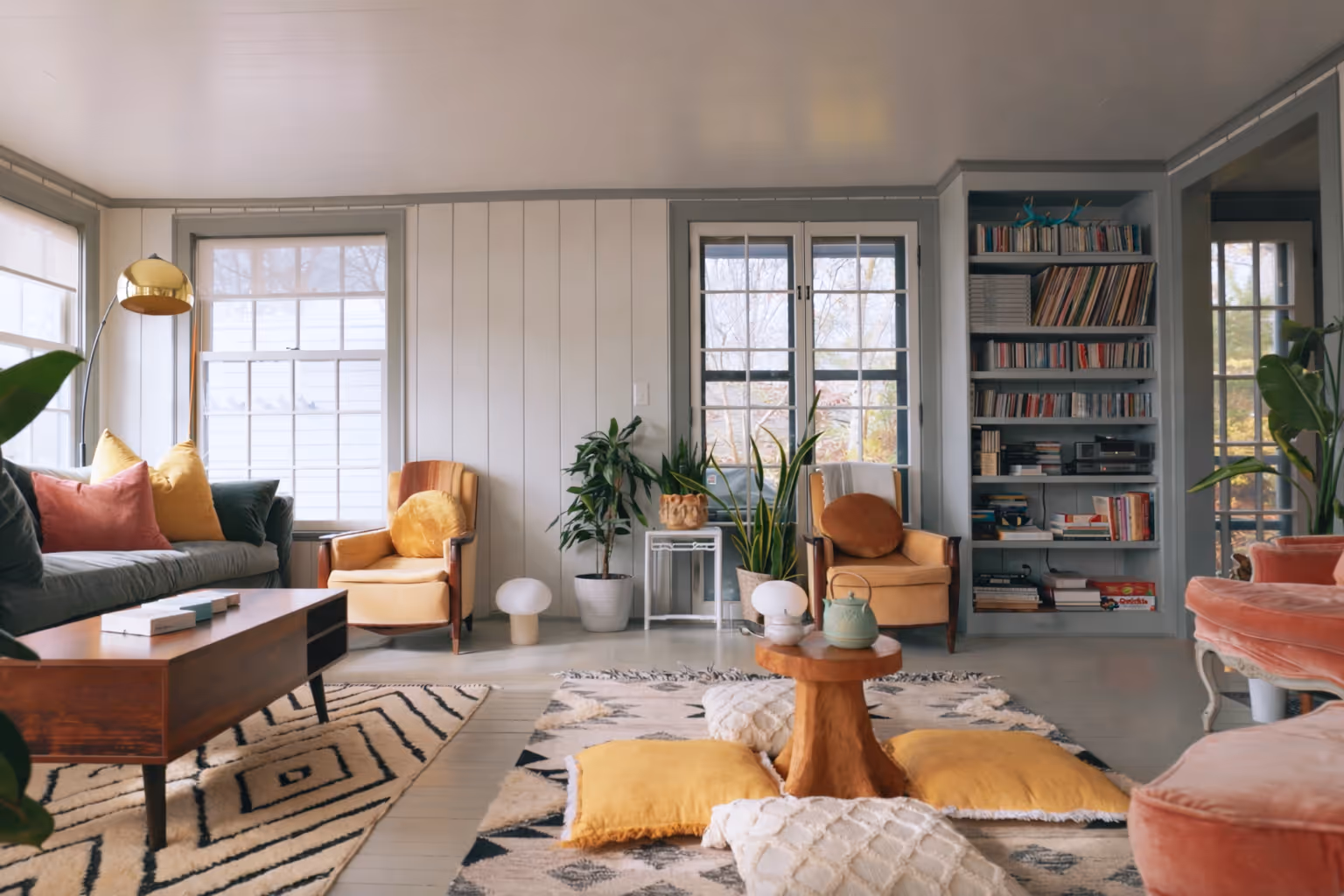 Cozy living room with yellow armchairs, a wooden coffee table, patterned rugs, and a built-in bookshelf filled with books and records.