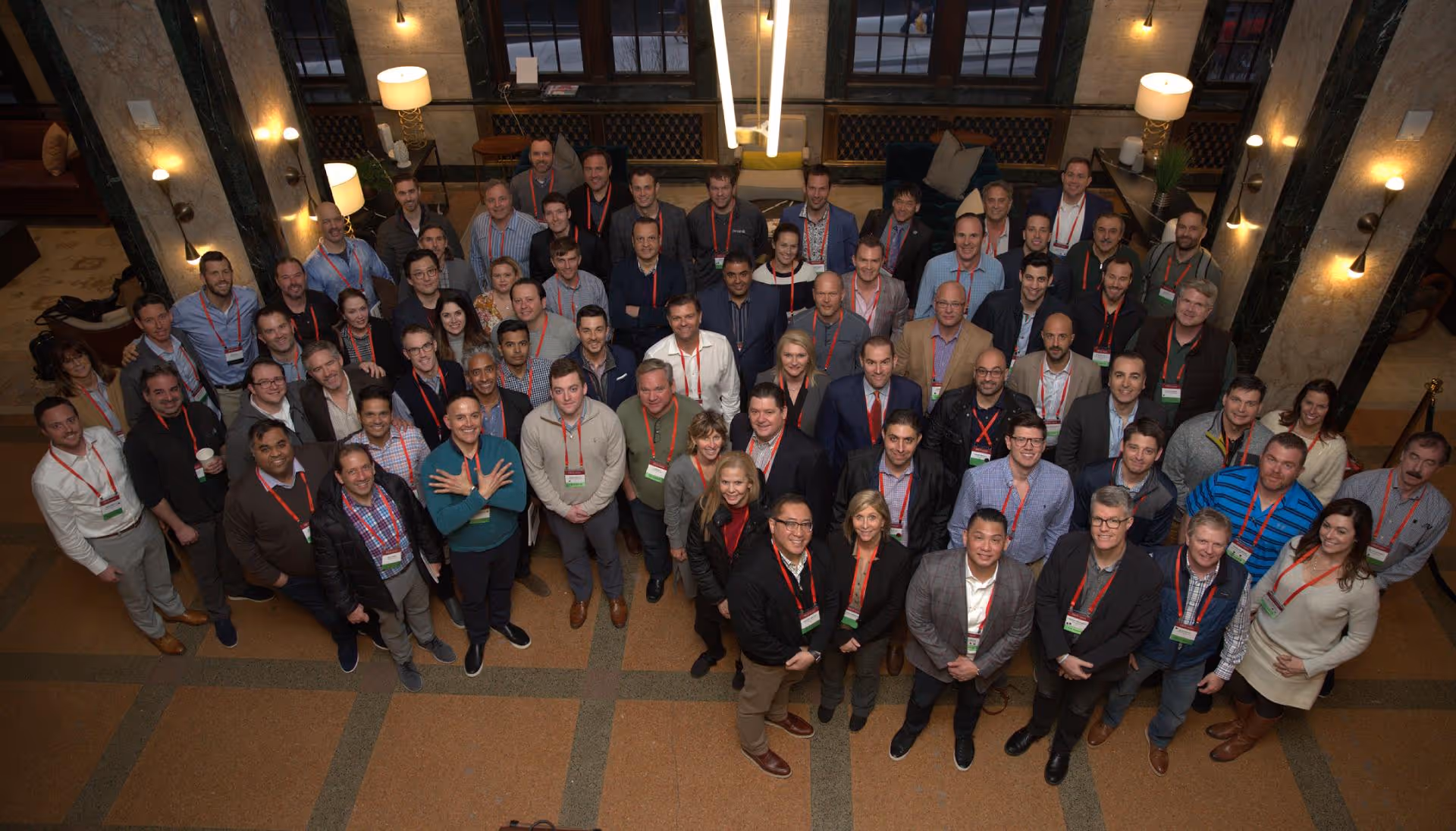 Large group of diverse conference attendees wearing name badges and red lanyards standing together in an indoor venue.