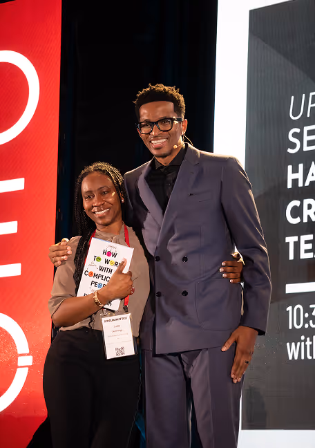 Two people smiling and posing together on stage at an event, one holding a booklet titled 'How to work with complicated people.'