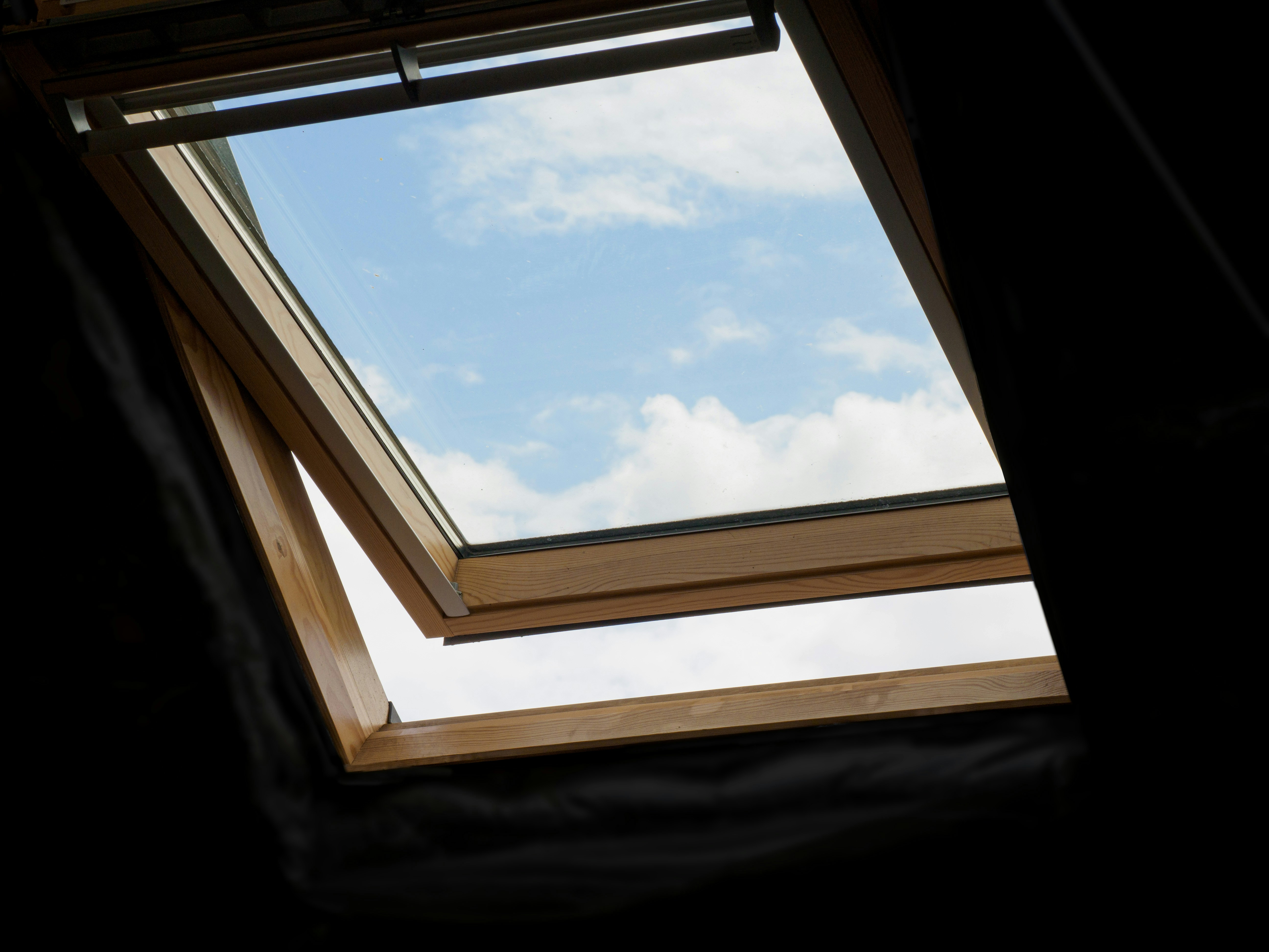 Open wooden-framed skylight window showing blue sky with scattered white clouds.