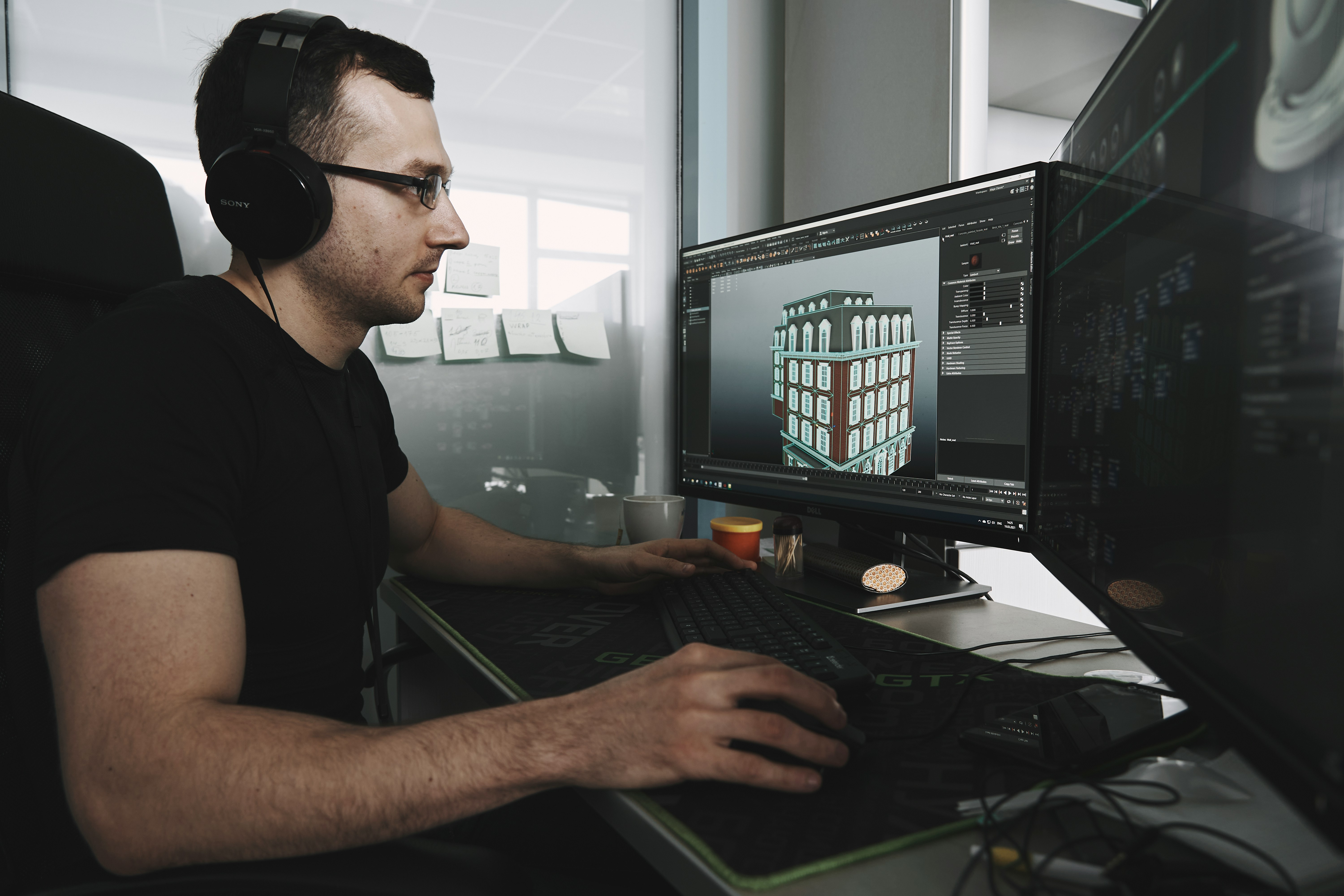 Man wearing headphones working on 3D building model on a computer in an office.