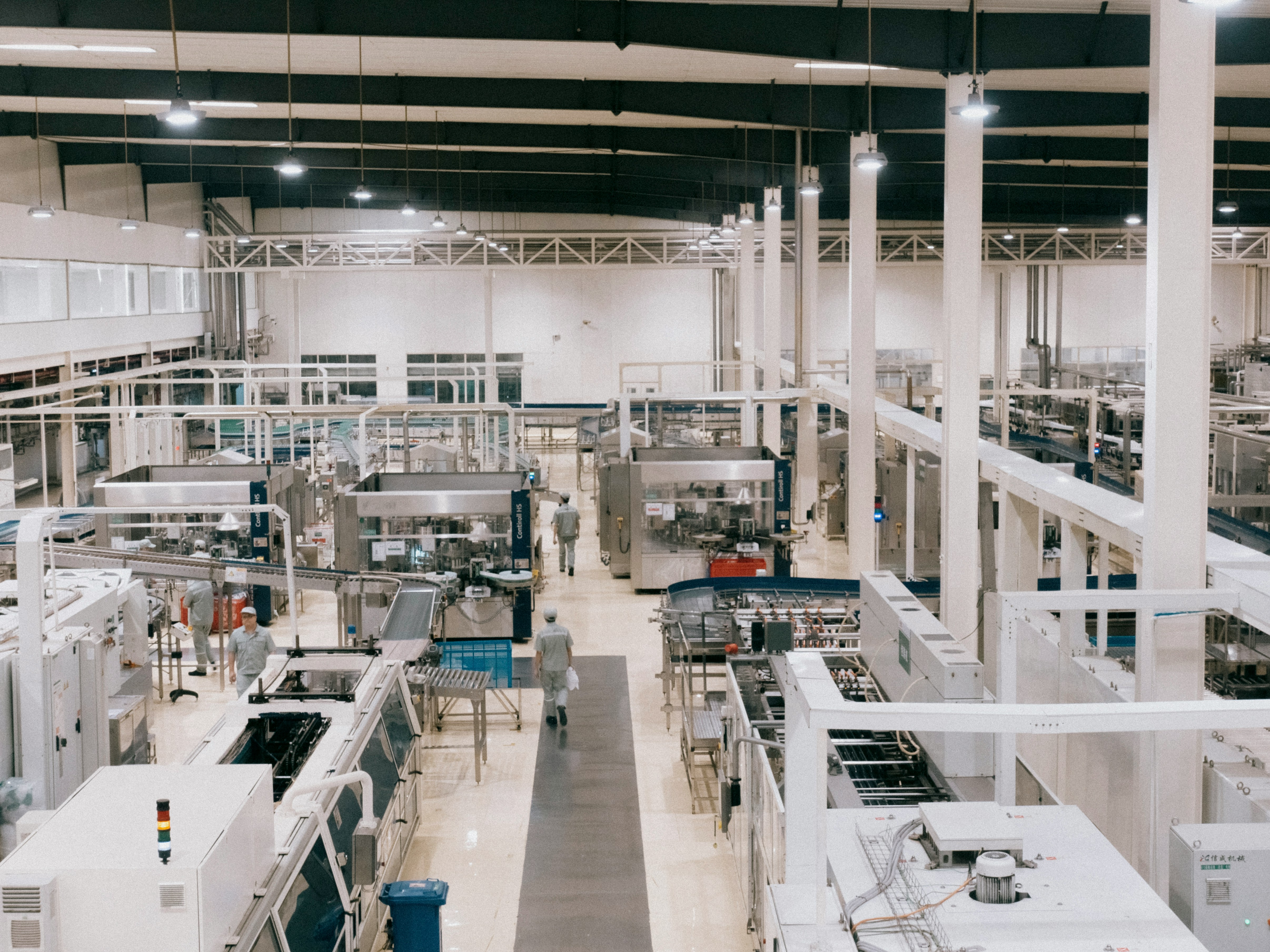 Wide view of a clean, modern factory floor with machinery and workers in uniforms walking around.