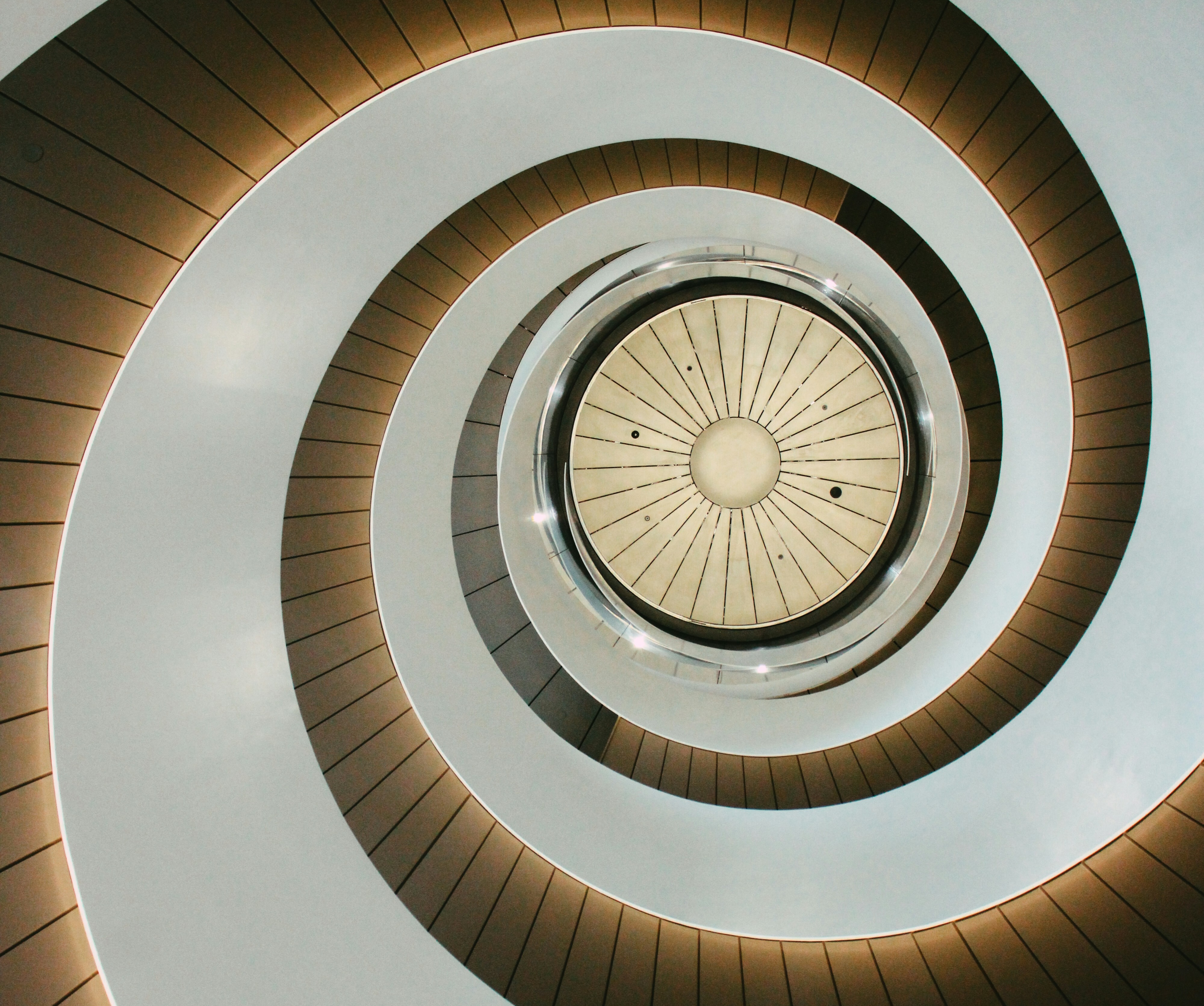 Looking up inside a modern spiral staircase with illuminated steps and a circular ceiling.