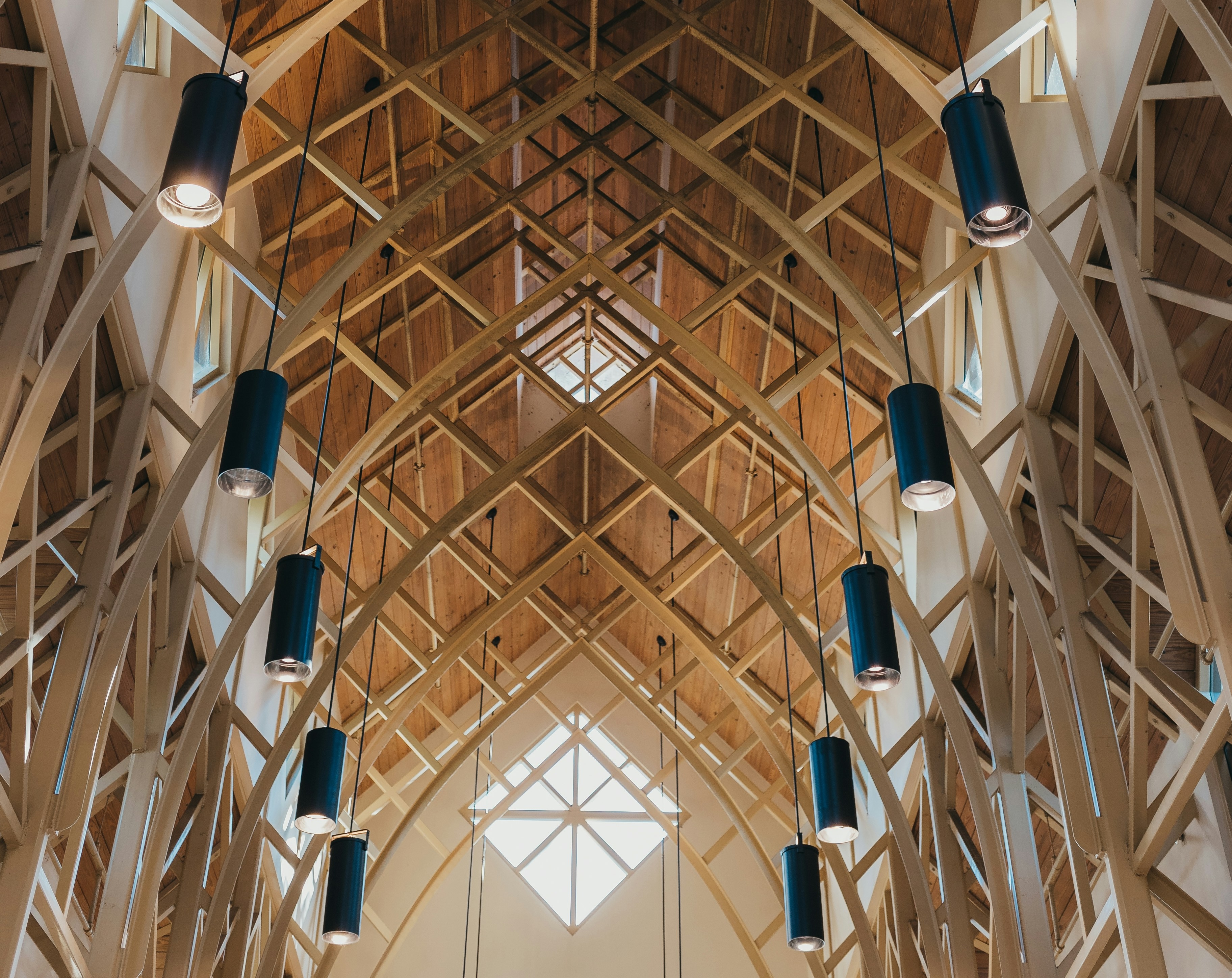 Wood ceiling with crisscrossed beams and hanging cylindrical black pendant lights in a large space.
