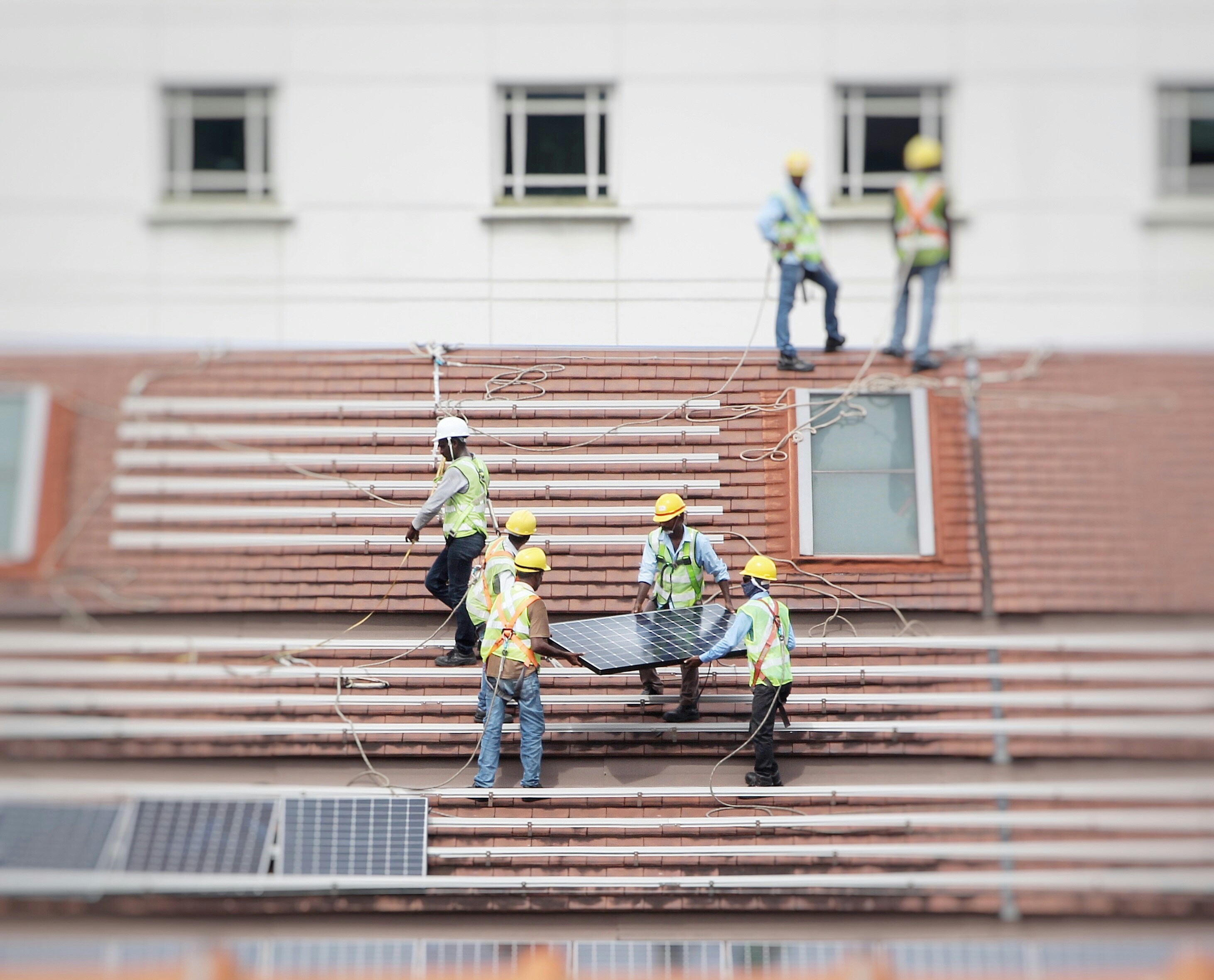 Workers in safety gear installing solar panels on a sloped roof with a skylight window.