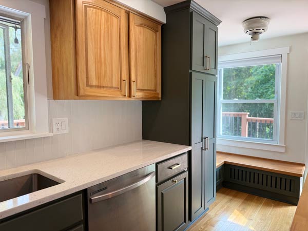 Bright kitchen with wooden cabinets, white dining table, chairs, and large windows letting in natural light.