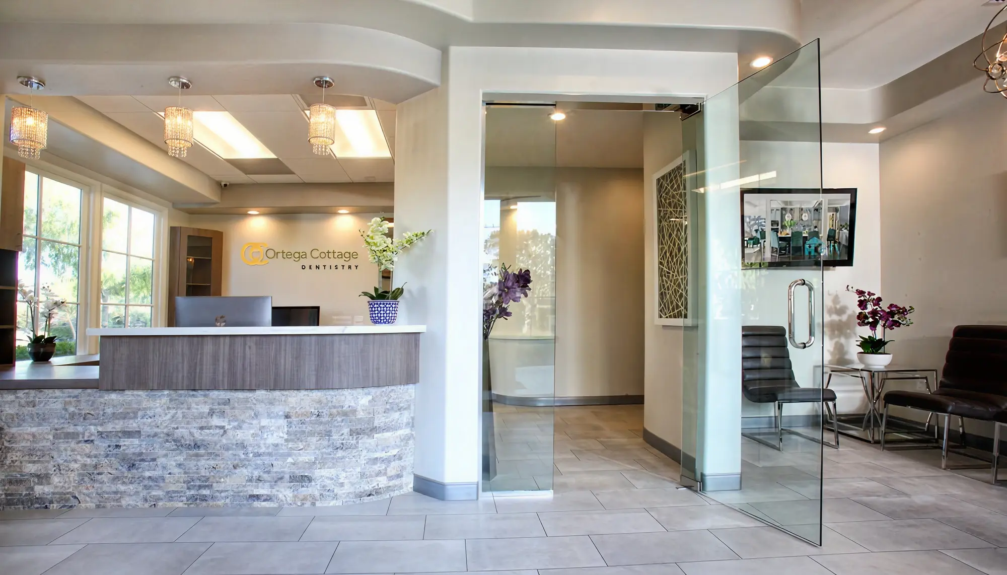 Full reception and waiting area at Ortega Cottage Dentistry with stone front desk, chandeliers, and patient seating