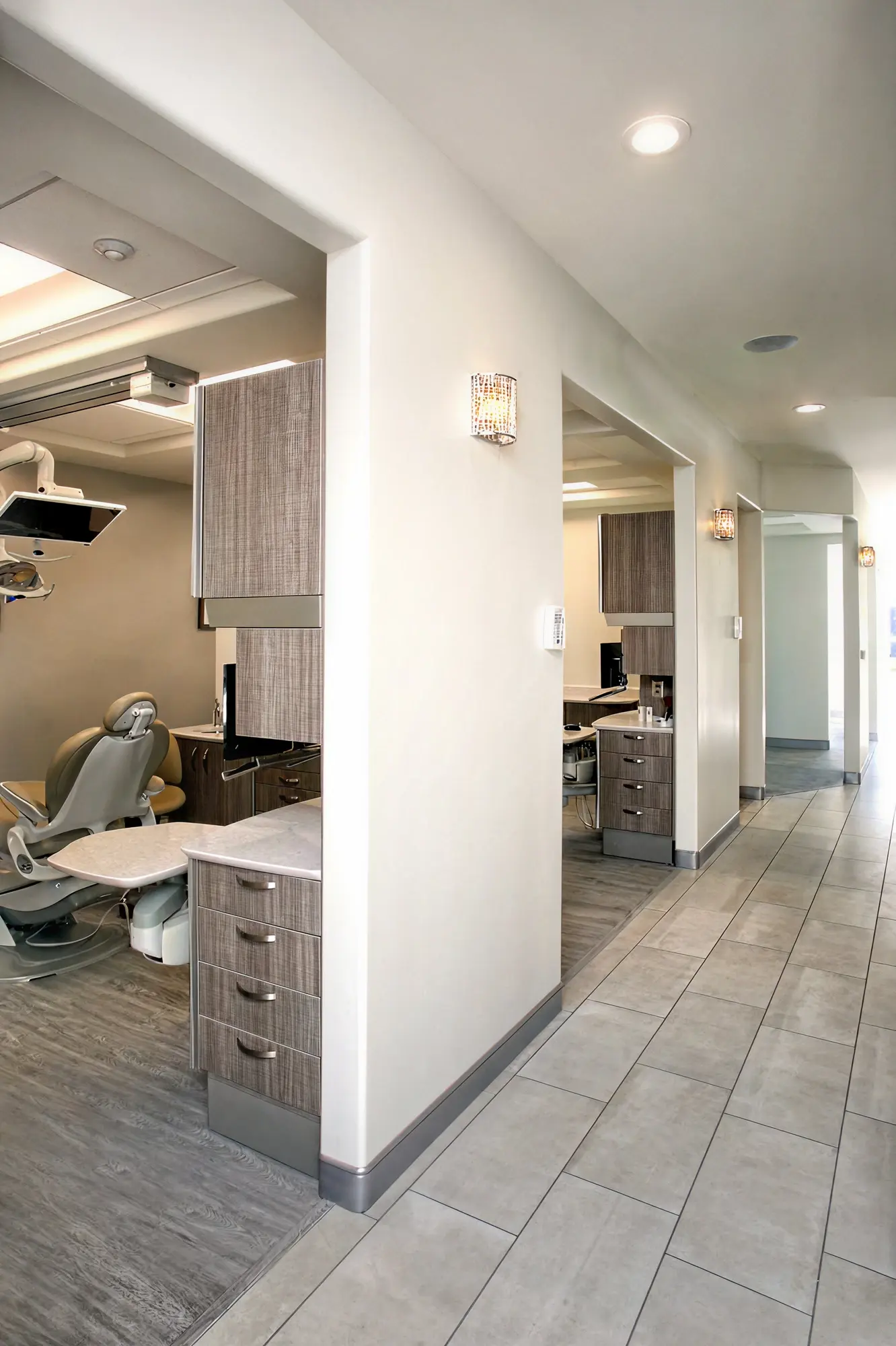 Hallway view of open dental treatment bays with patient chairs and crystal wall sconces at Ortega Cottage Dentistry