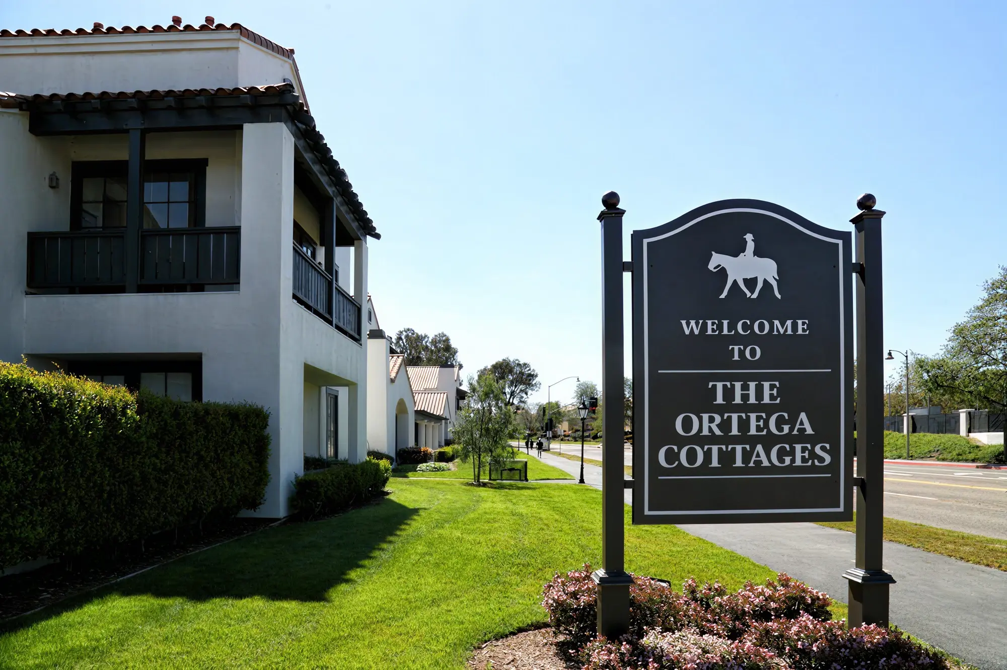 Welcome to the Ortega Cottages monument sign with Spanish-style buildings and landscaped grounds