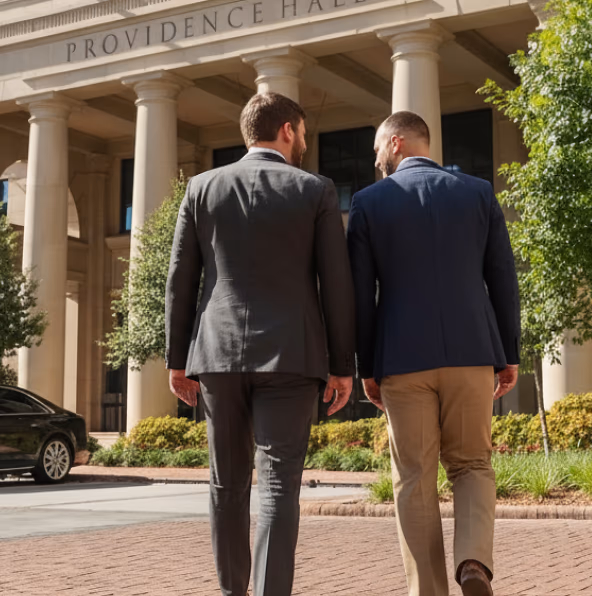Two men in business attire walking and talking outside a building with large columns labeled Providence Hall.