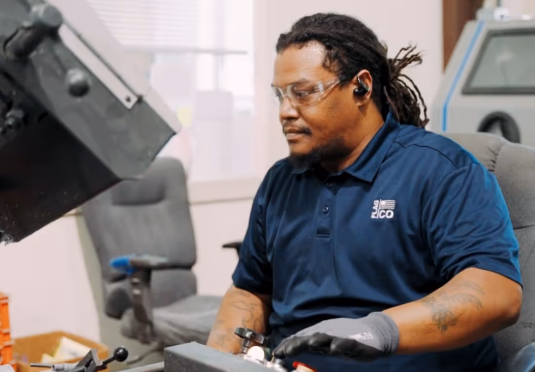 Man wearing safety glasses and gloves operating industrial machinery in a workshop.
