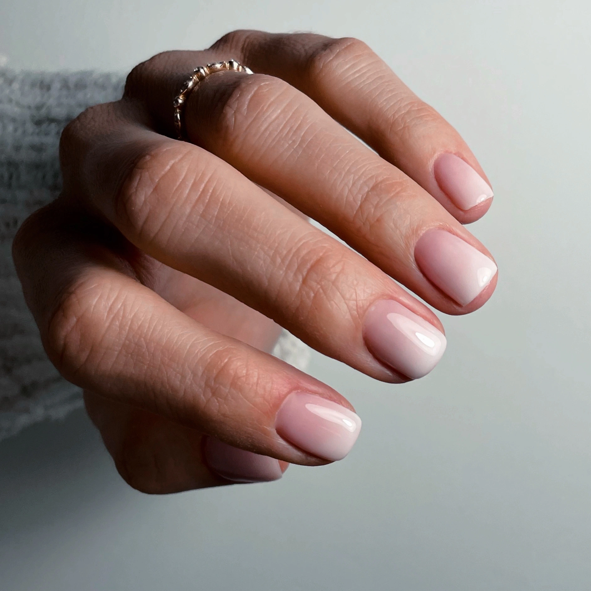 Gros plan sur une main aux ongles courts soigneusement manucurés, vernis d'un gel rose pâle brillant.