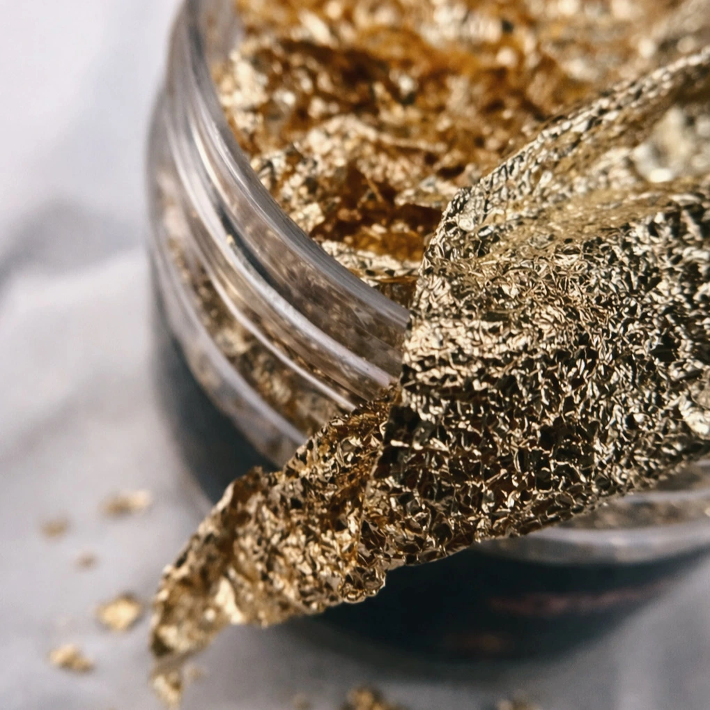 Gros plan sur des paillettes dorées brillantes en train d'être déposées ou retirées d'un récipient transparent.