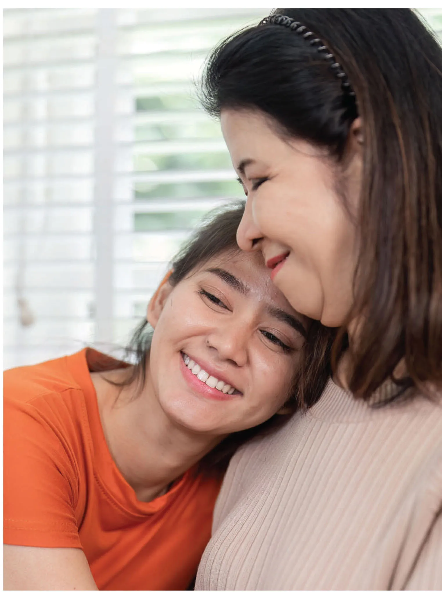 Young woman smiling and leaning her head against an older woman in a close warm embrace.