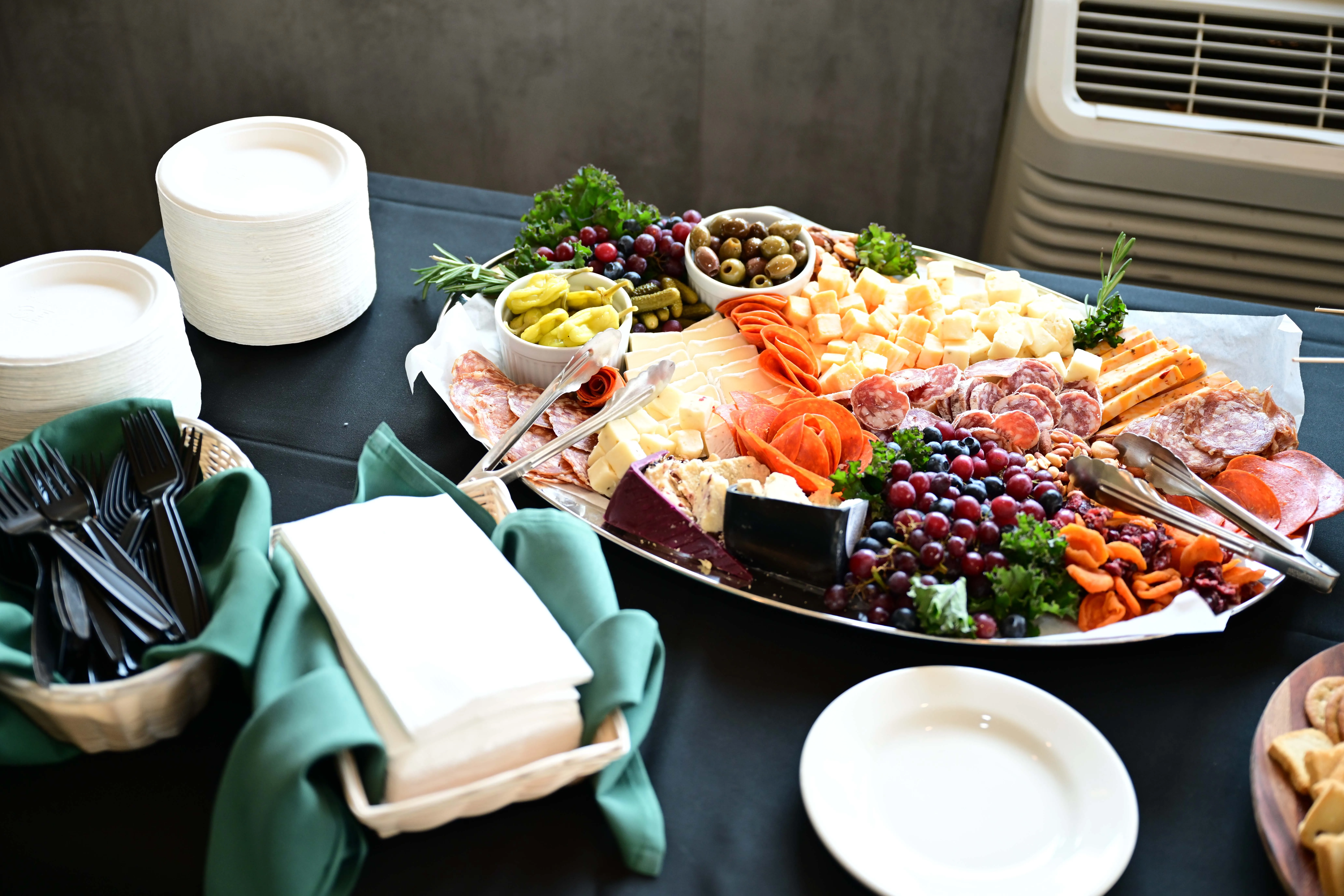 Charcuterie platter with assorted cheeses, meats, olives, grapes, and dried apricots on a black tablecloth.