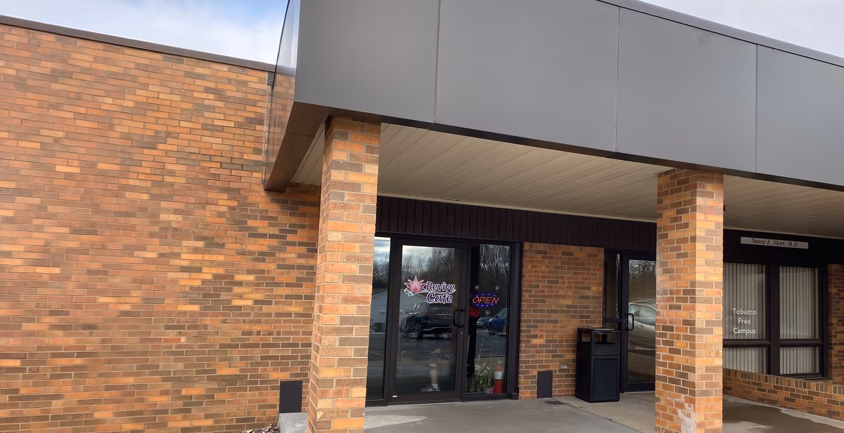 Entrance to Revive Cafe with glass double doors and an open sign, located in a brick building with pillars.