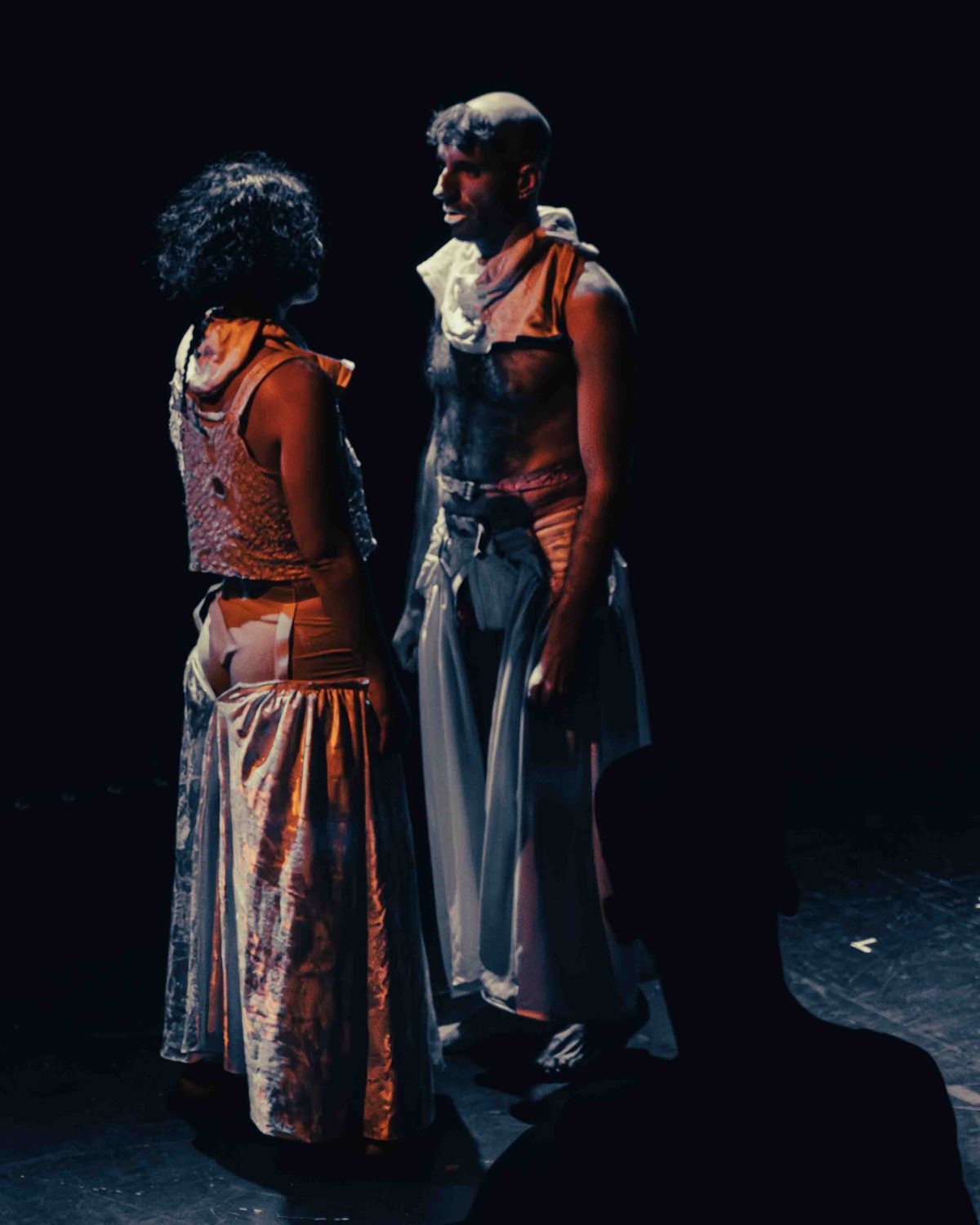 Two performers in deconstructed wedding gowns facing each other on a dark stage