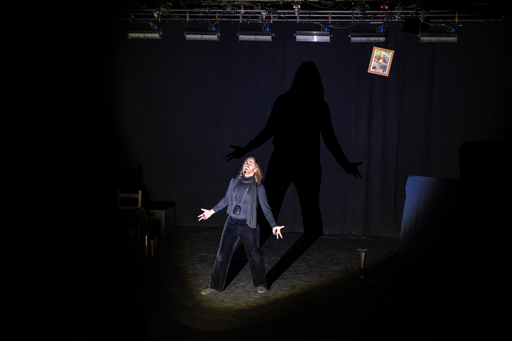 Isaac Kessler in 1-Man No-Show at Montréal Fringe 2026 — figure stands under a wide spotlight with a large shadow projected on the backdrop.