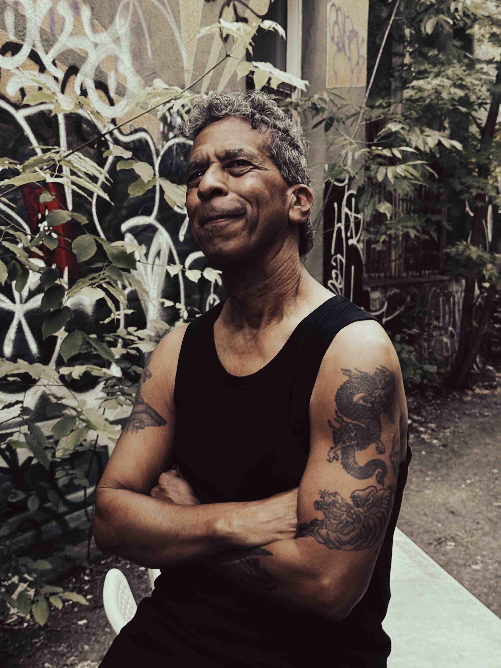 Michael Gougis sits outdoors with arms crossed and a playful smile, leaning slightly to one side.
