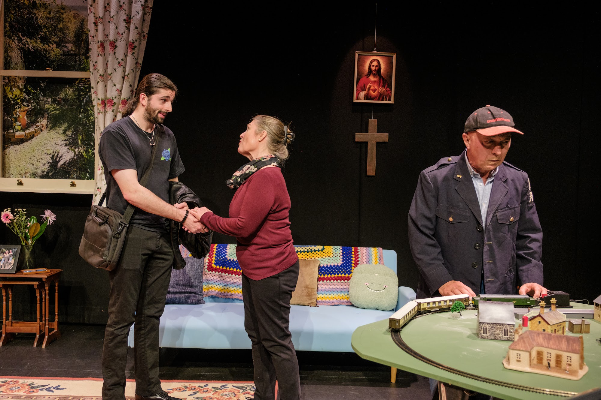 A mother shakes hands with a young man in front of a grandfather who watches closely.
