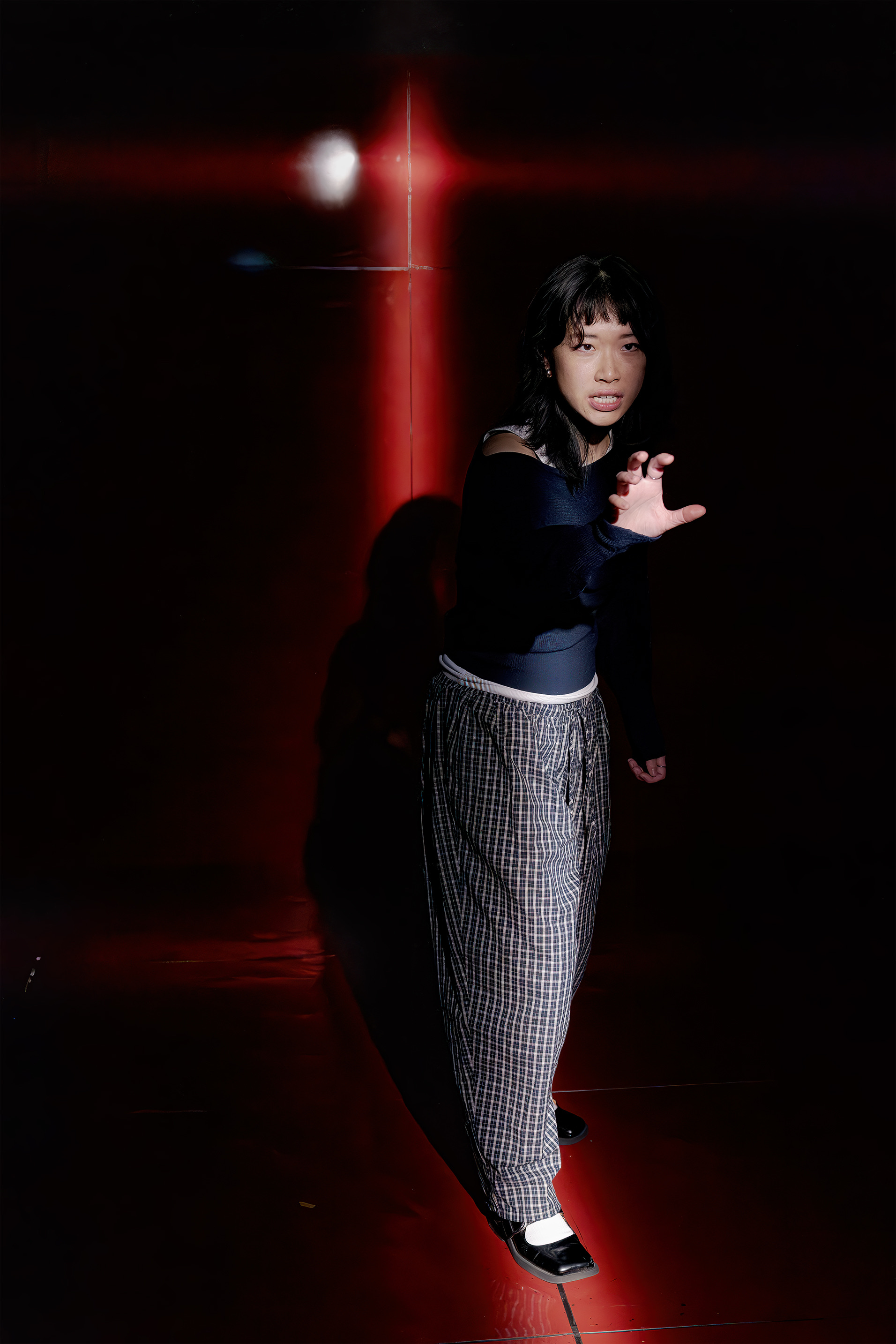 Claudia stands firmly with her arm outstretched and an assertive expression, framed by red lighting.