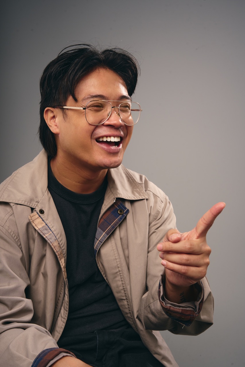 Esky smiles and gestures with both hands, leaning slightly forward as if engaging with an audience.