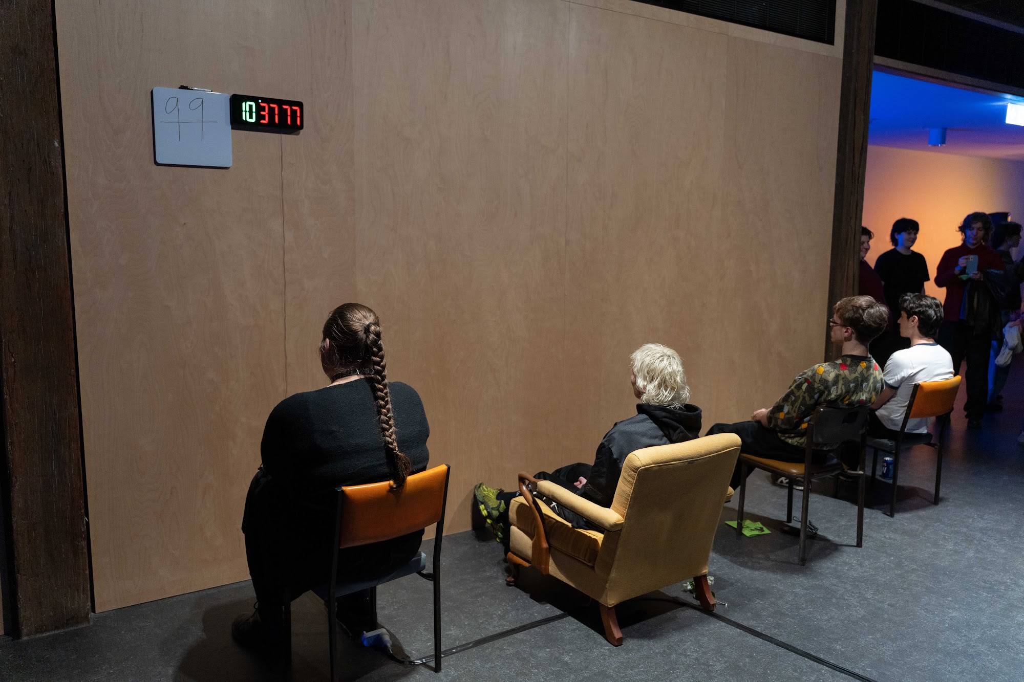 The line of five chairs facing the plywood wall in Wallmaxx with me at Artspace, Kudos Live: G R / N D 2026.