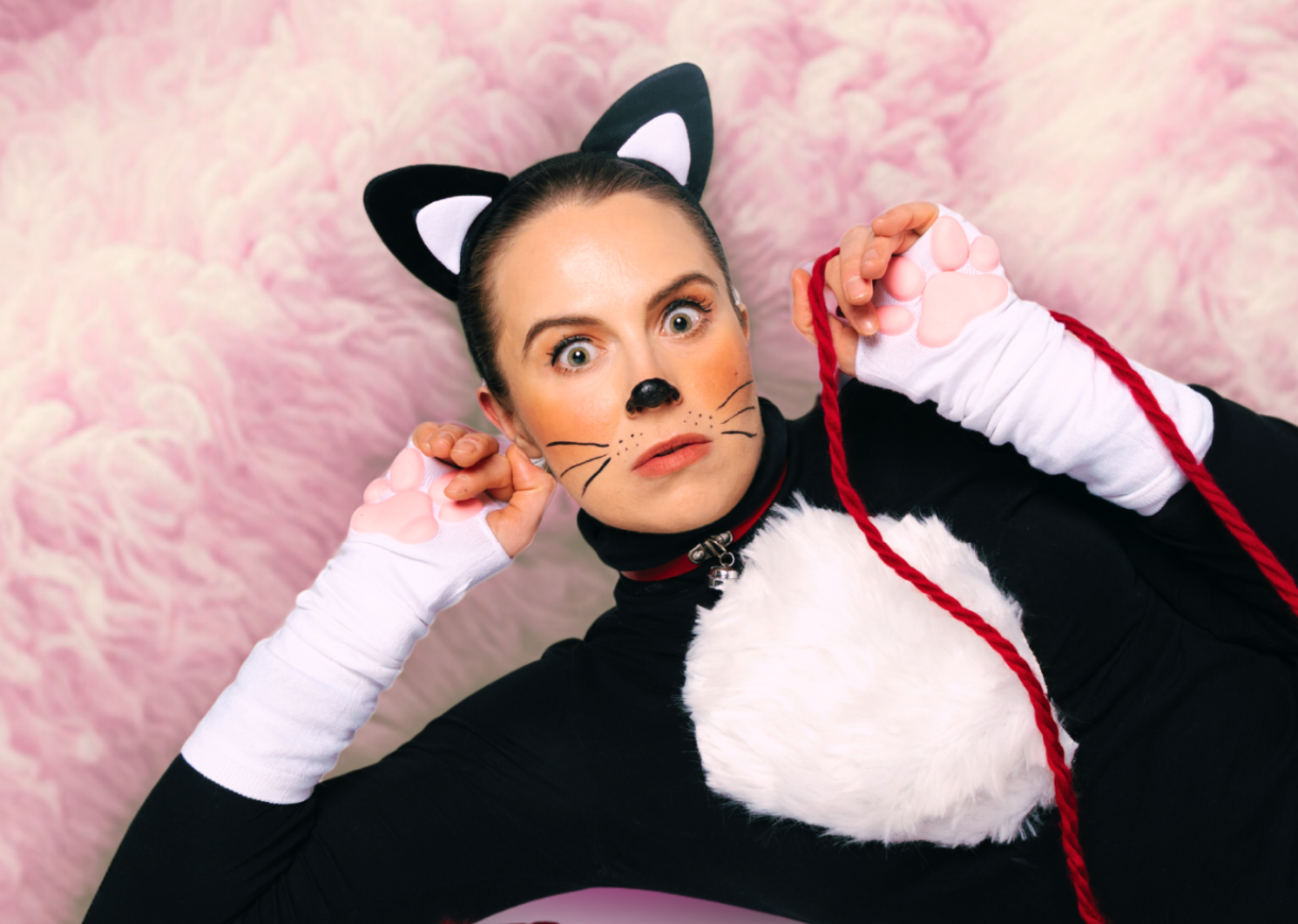 A lady dressed in a fur cat suit with whiskers and nose painted on is holding a piece of red string.