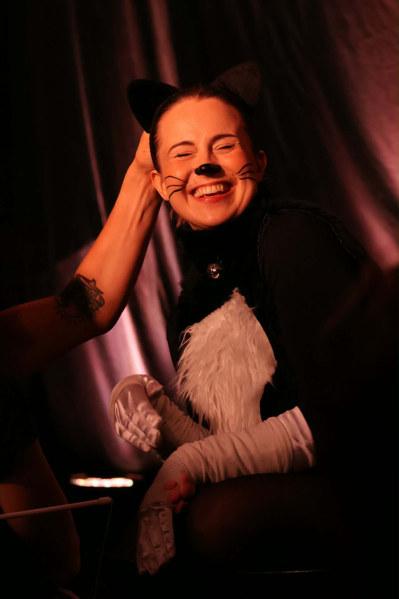 A woman dressed as a cat happily smiling as her head is rubbed.