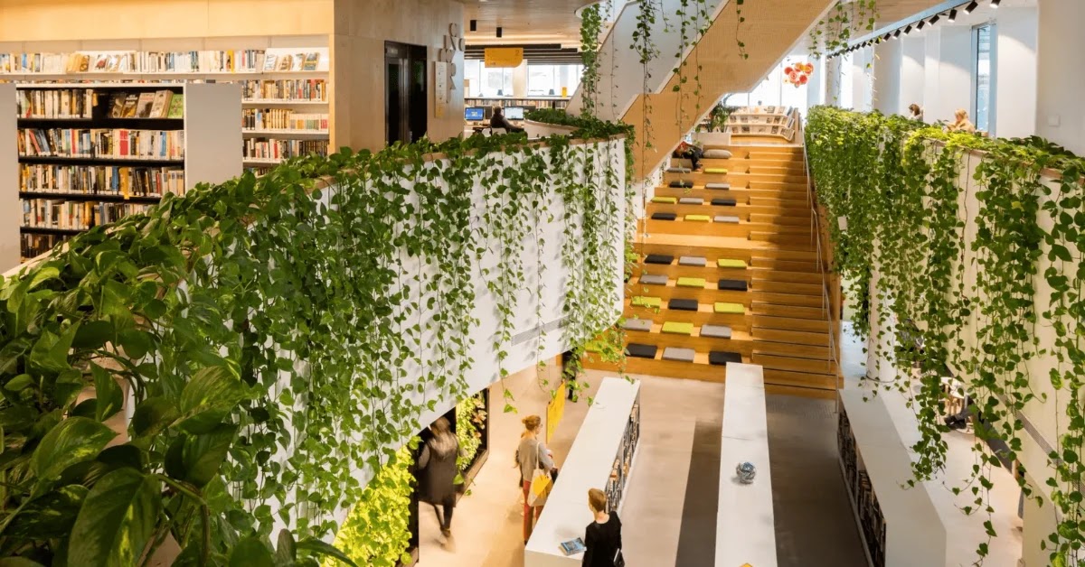 Birdseye view of level 1 of Woollahra Library from level 2 showing the forum steps, bookshelves, and people browsing. Hanging plants cascade from the second level banisters.
