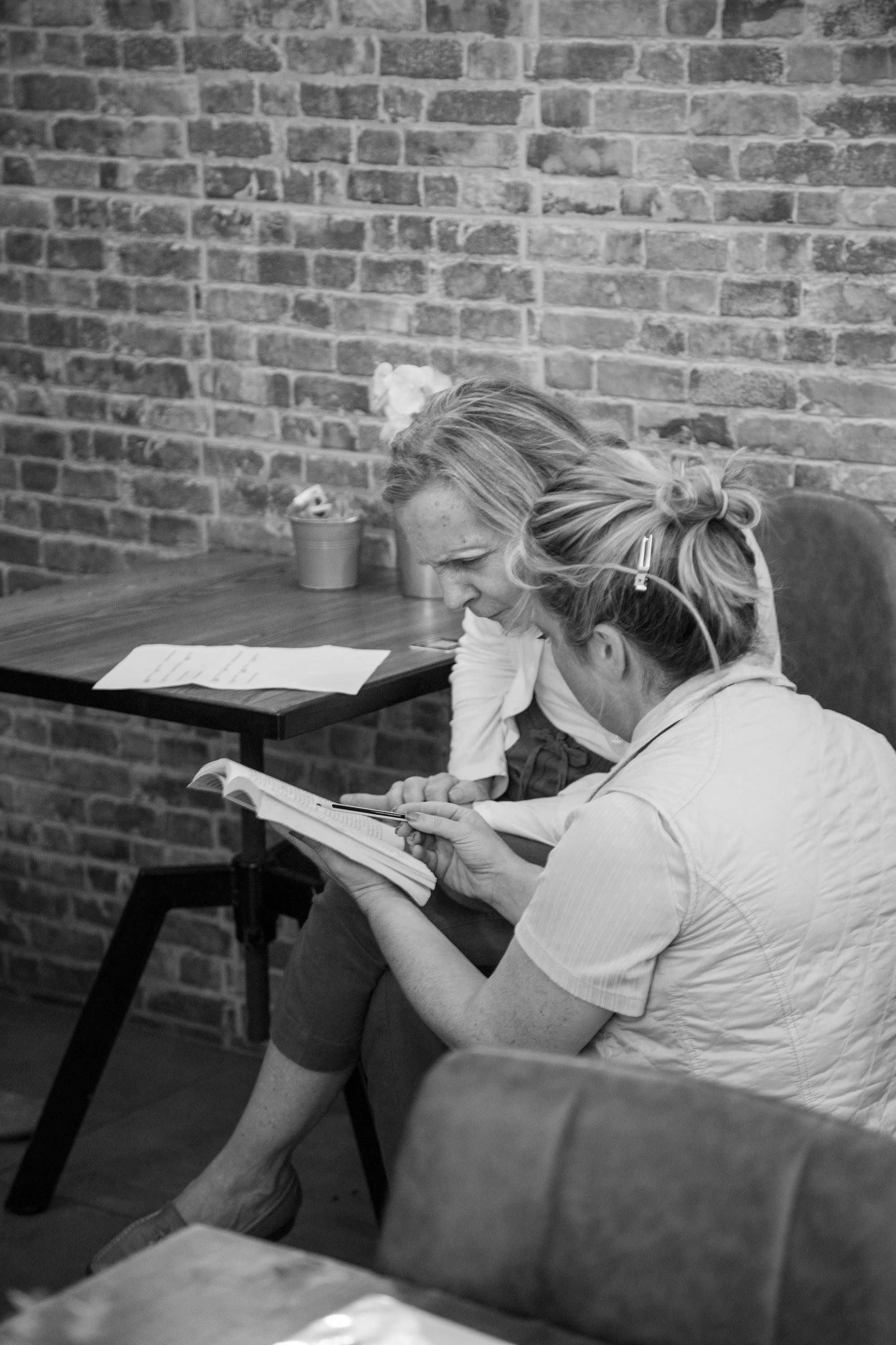 Sophie Dillman sits in a chair in front of a brick wall. She is wearing a blue dress and leaning against a cafe table with a flowerpot on it.