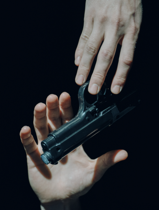 A hand reaches for a gun from the bottom of the frame. A hand from above offers the gun.
