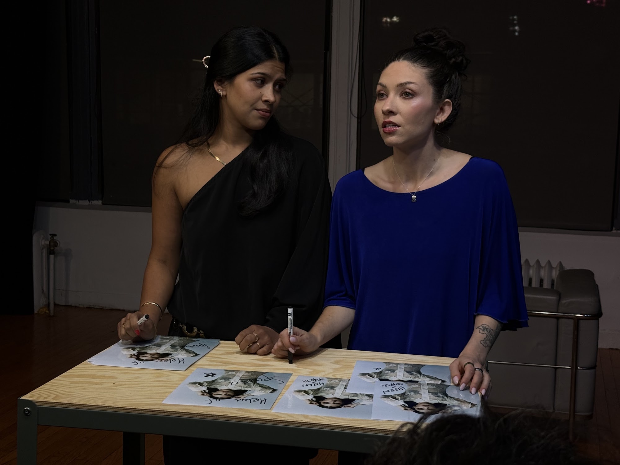 Two women, one in a red dress and the other in a black top, are looking through binoculars.