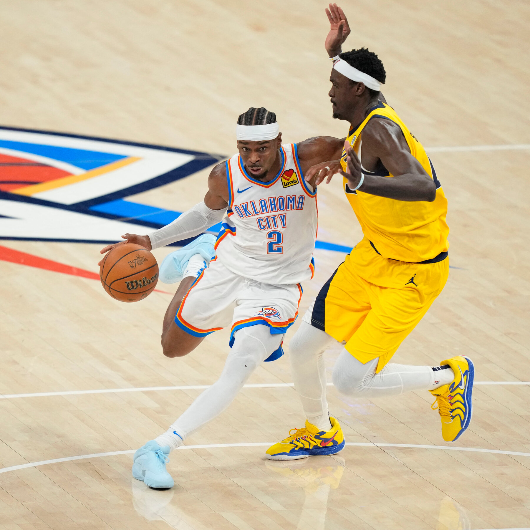 Basketball player in Oklahoma City jersey dribbling the ball while guarded by a player in a yellow jersey on a basketball court.