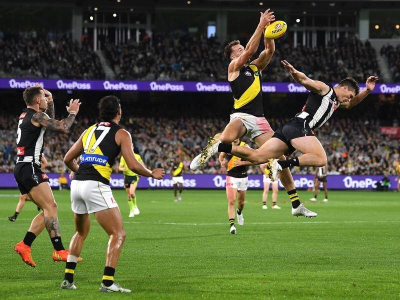 Two Australian rules football players jumping to catch the ball mid-air during a match with a stadium crowd in the background.