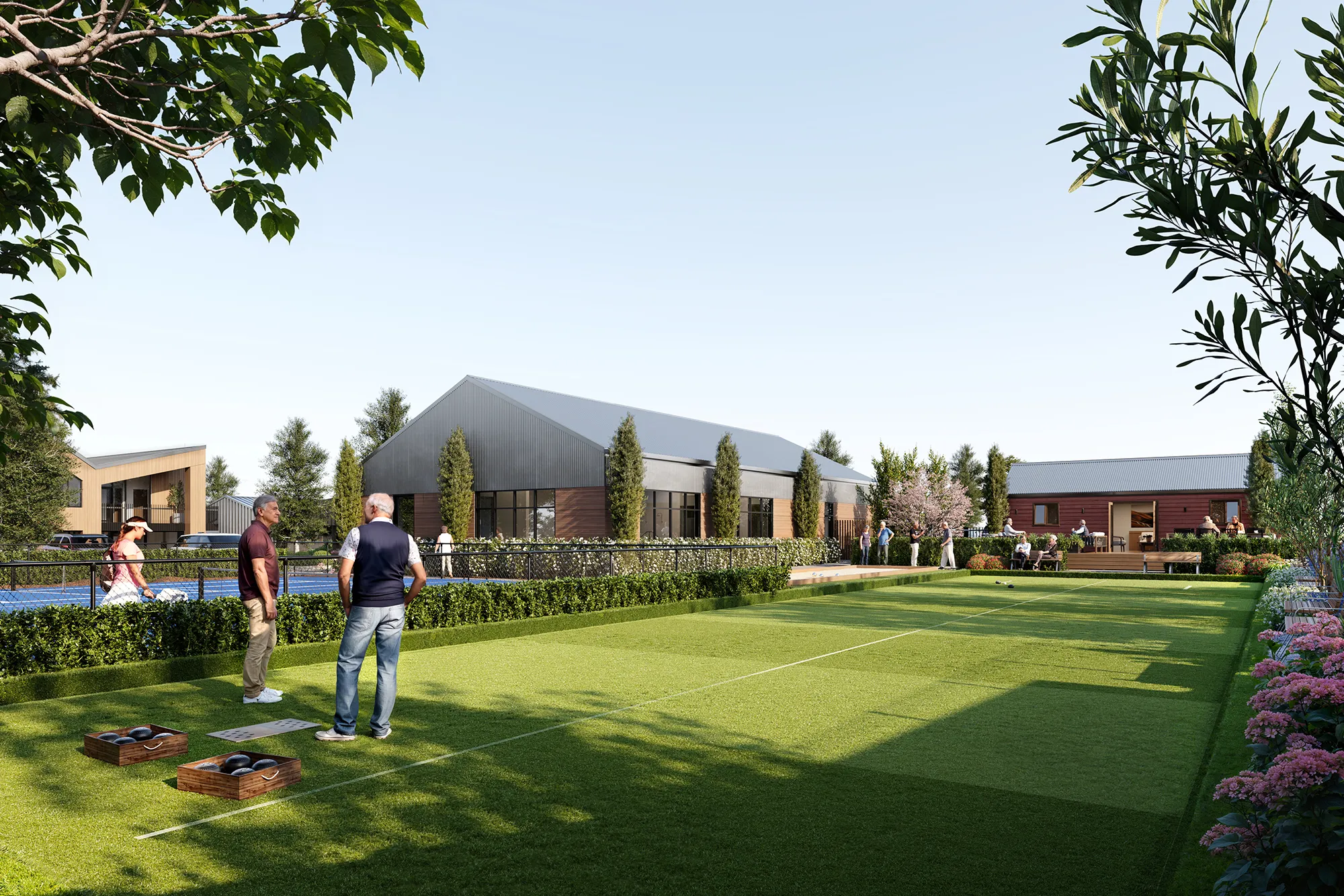 People playing bowls on a green lawn surrounded by modern buildings, trees, and flower beds under a clear sky.