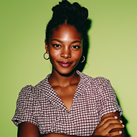 Confident woman with braided hair wearing a checkered blouse against a green background.